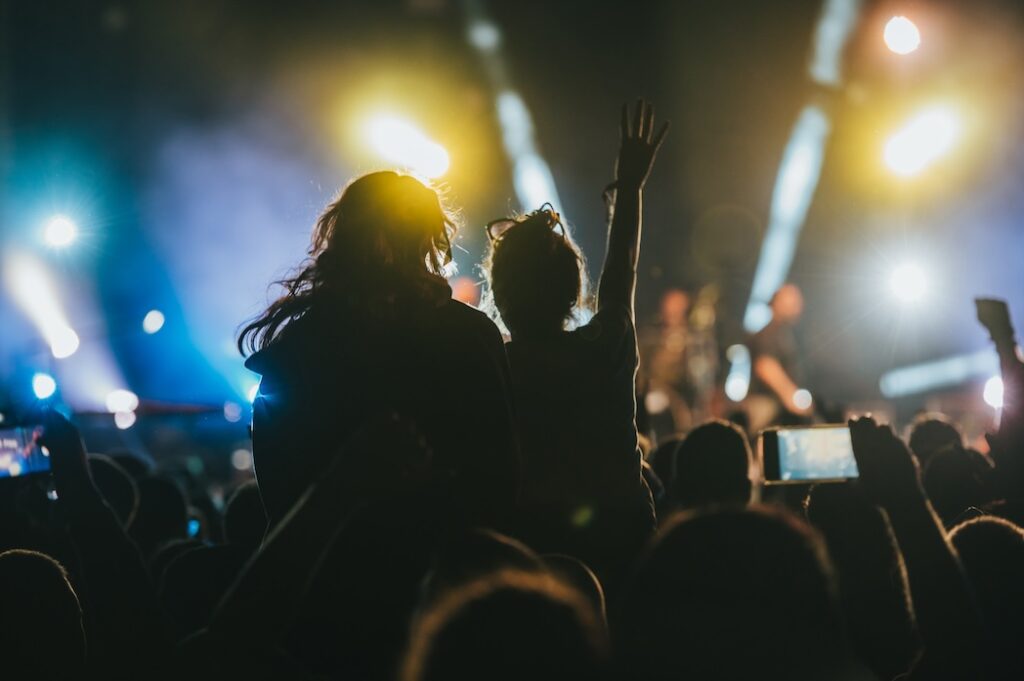 Two cheerful females having a good time while dancing in the crowd on a concert. Youth and celebration concept. Back view.